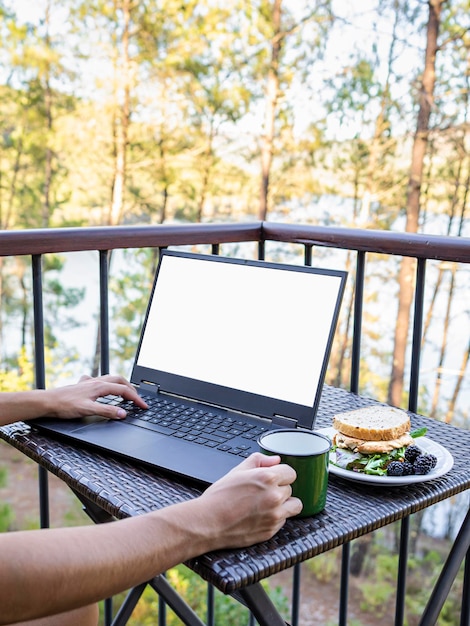 Girl39s arms teleworking on a terrace in front of a forest and a lake digital nomad teleworking