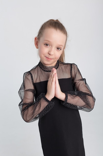 The girlchild covers her face with her hands in surprise and looks dreamily away A little baby in a black dress Children's goods clothing and accessories Expressive emotions on the face