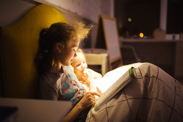 Girls best friends read fairy tale before sleep. Best books for kids. Sisters read book in bed. Family tradition.