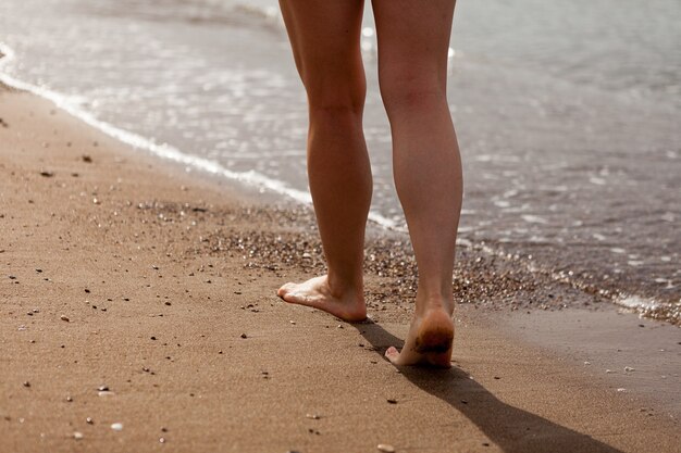 A girls feet walking on the sand along the sea coast sand and sea water the girl walks on the sand stop closeup