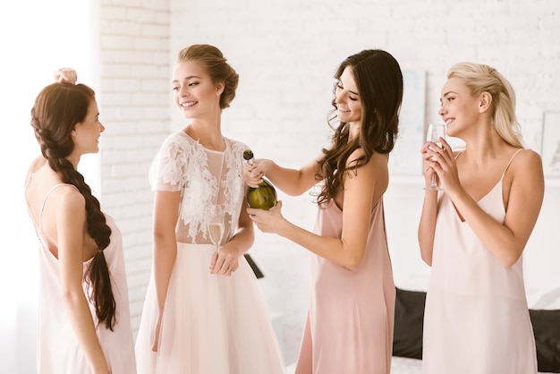 Girls having fun. Cheerful laughing young girls standing in the white bedroom while having fun and drinking alcohol