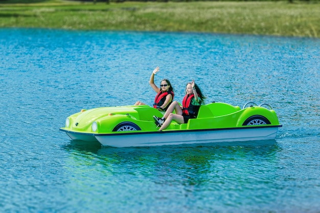 Girls in safety jackets wave and ride a pedal boat on a mountain lake