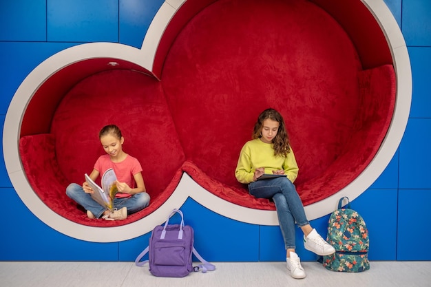 Girls sitting with book and tablet resting after school