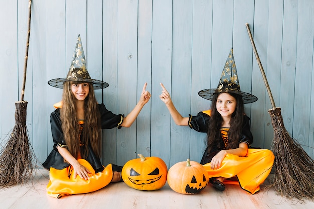 Girls in witch costumes with brooms sitting by fence