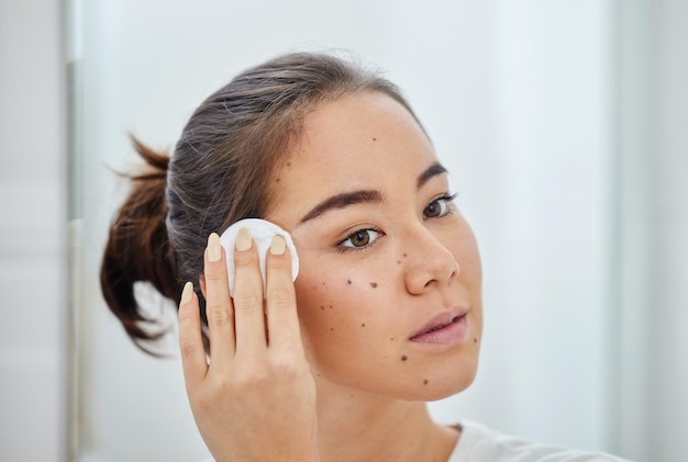 Give your skin the love it deserves Shot of a young woman cleaning her face with a cotton pad in a bathroom at home