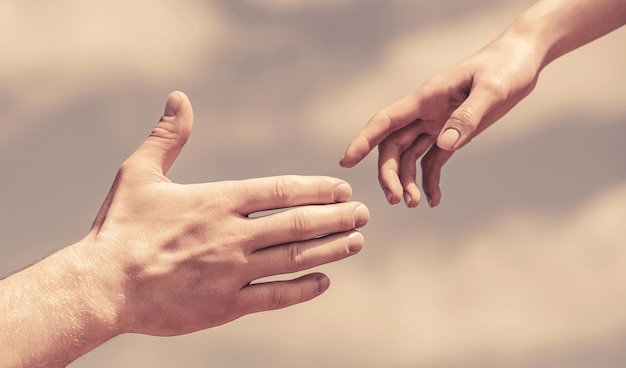 Giving a helping hand Hands of man and woman on blue sky background Lending a helping hand Hands of man and woman reaching to each other support Solidarity compassion and charity rescue