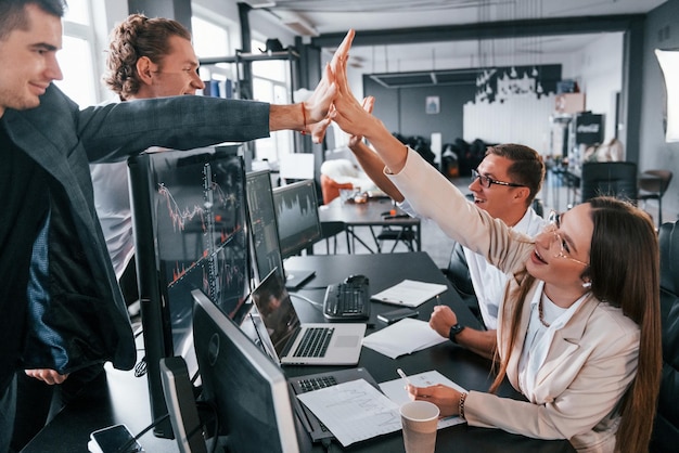 Giving high five Team of stockbrokers works in modern office with many display screens