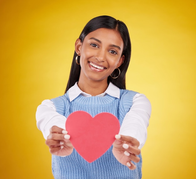 Giving paper and heart with portrait of woman in studio for love support and romance Valentines day kindness and date with female and symbol on yellow background for health happiness and hope