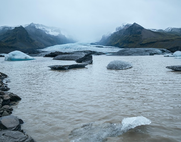 Glacier tongue slides from Vatnajokull icecap or Vatna Glacier near subglacial Oraefajokull volcano Iceland Glacial lagoon with ice blocks and surrounding mountains