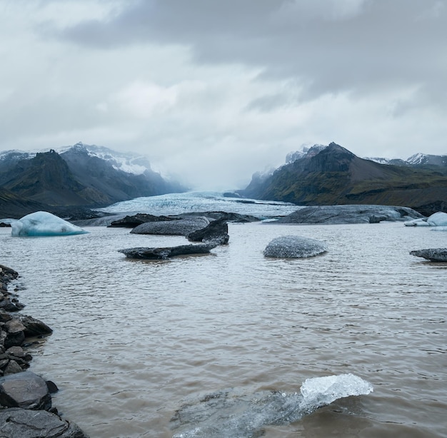 Photo glacier tongue slides from vatnajokull icecap or vatna glacier near subglacial oraefajokull volcano iceland glacial lagoon with ice blocks and surrounding mountains