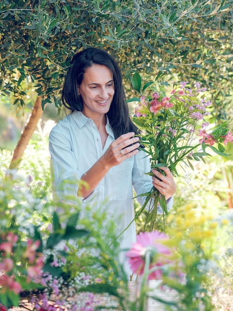 Glad brunette in white shirt creating bouquet of gentle flowers on sunny day in nature