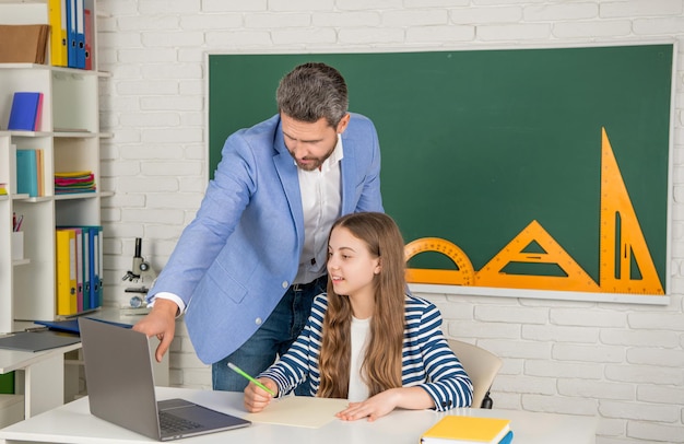 Glad child with teacher in classroom use laptop