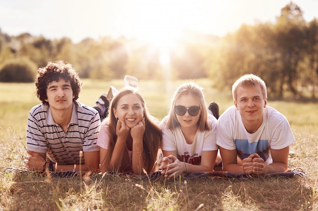 Glad four friends with happy expression lie on grass