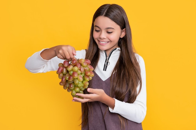 Glad girl hold fresh grapes fruit on yellow background