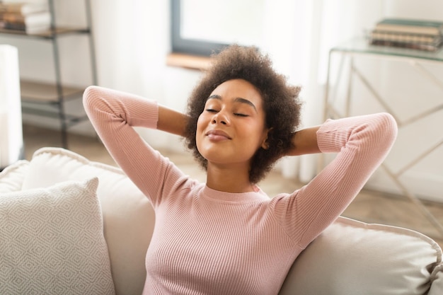 Glad happy young mixed race woman resting on sofa with closed eyes enjoy peace silence and free time