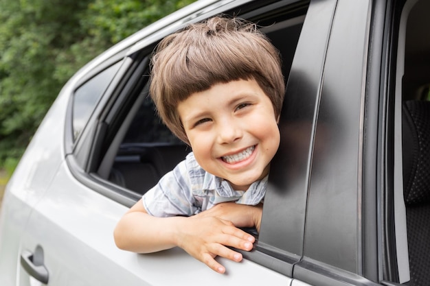 Glad little kid looks out the open window and enjoys trip with his parents in car outdoors in summer