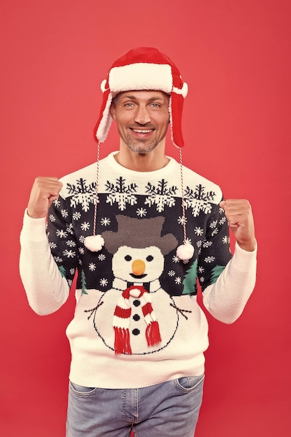 Glad man in winter sweater and hat celebrating holiday n red background christmas