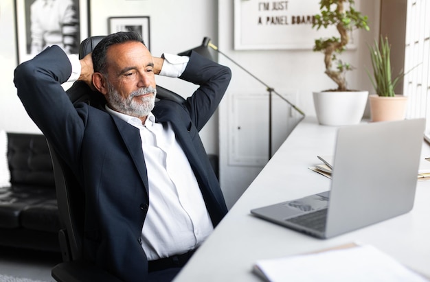 Glad positive caucasian senior businessman in suit resting looking at computer in modern office