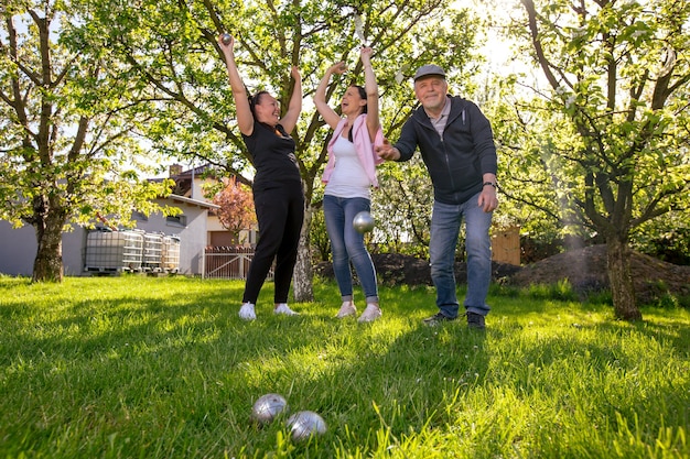 Glad positive smiling family playing French traditional game petanque in a garden outside during lovely summer day enjoying leisure time