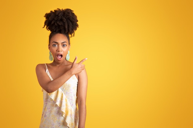 Glad shocked millennial black lady with open mouth pointing finger at copy space