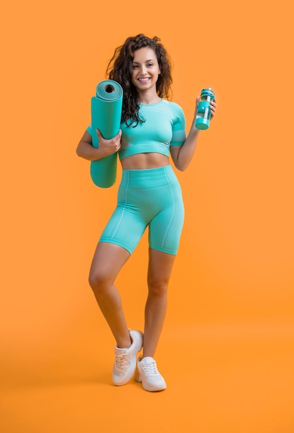 Glad sportswoman in sportswear with fitness mat and sport bottle in studio fitness sportswoman