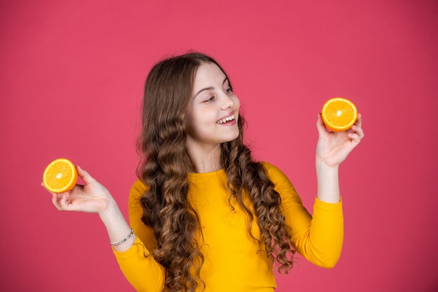 Glad teen child hold orange fruit on pink background