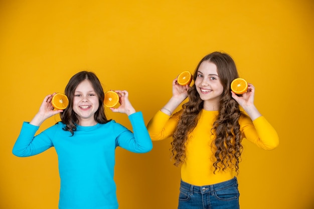 Glad teen children hold orange fruit on yellow background