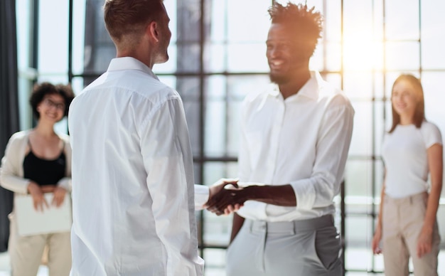 Glad to work with you Young modern men in smart casual wear shaking hands and smiling while working in the creative office