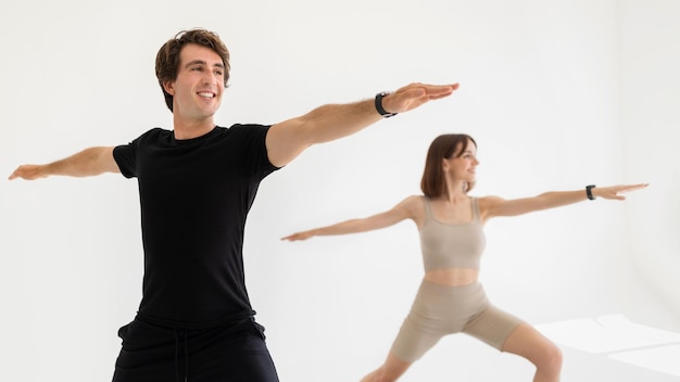 Glad young european man and lady in sportswear exercising for hands practicing yoga in gym