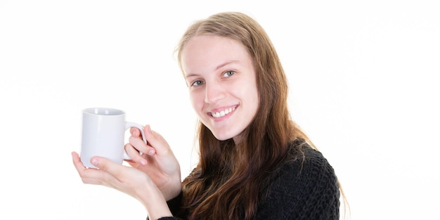 Glad young woman holds mug with coffee enjoys spare time stands against white background copy space area