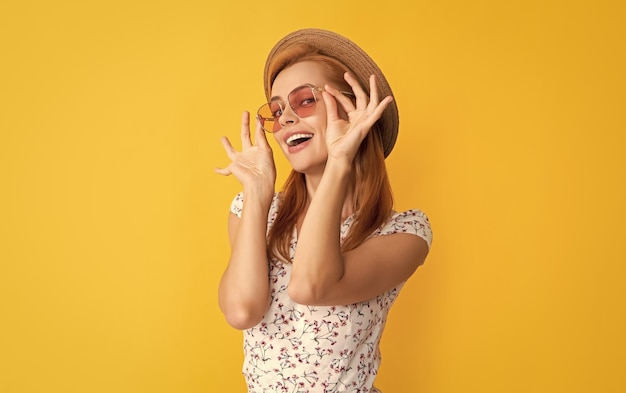 Glad young woman in straw hat and sunglasses on yellow background