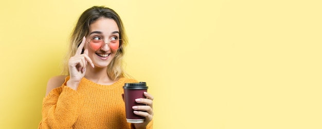 Glamor woman in glasses in an orange sweater with a drink of coffee on a yellow background