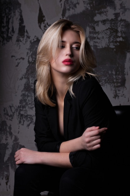 Glamor young woman with pink lips wearing black jacket posing at studio with shadows