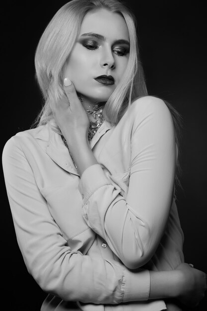 Glamorous blond model posing at studio with bright makeup and foil on her neck. Monochrome shot