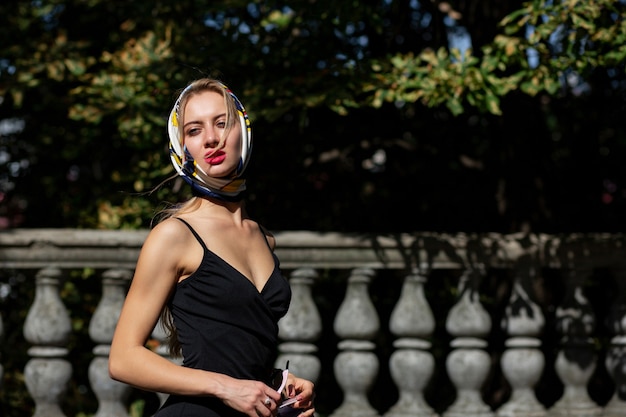 Glamorous model with red lips wearing shawl and black dress posing with sun light. Space for text