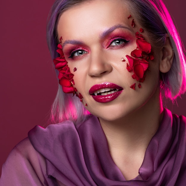 Glamorous vampire look with bright pink eye shadow and flower petals on the skin