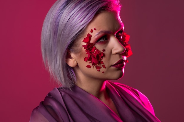 Glamorous vampire look with bright pink eye shadow and flower petals on the skin