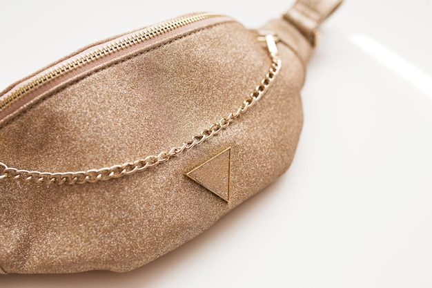 Glamorous women's belt bag of golden color on a white isolated background. Fashion handbag with a gold chain. Close-up.