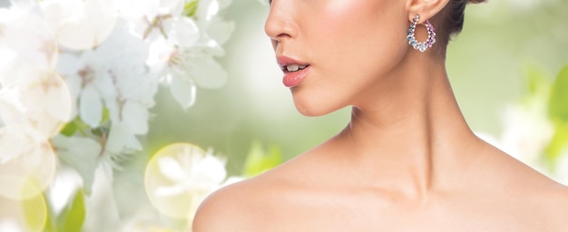 glamour, beauty, jewelry and luxury concept - close up of beautiful woman face with earring over natural spring cherry blossom