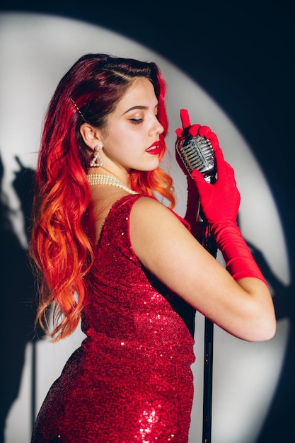 Glamour red haired lady singing with microphone on the dark stage background