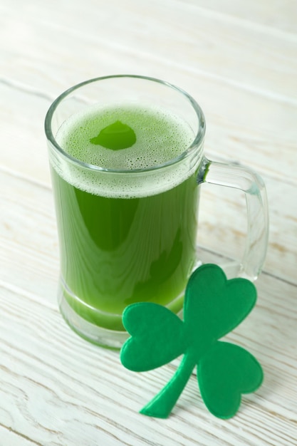 Glass of ale and clover leaf on white wooden table