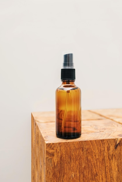 Glass amber natural oil or serum bottle and wooden stool against gray bathroom background with copy space Eco friendly sustainable zero waste cosmetic product for skin care