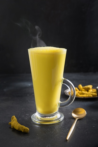 Glass of ayurvedic golden turmeric latte milk with curcuma powder on black . Vertical .