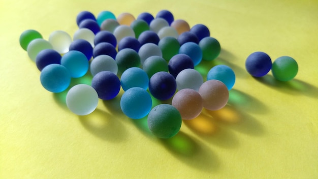 Glass balls of different colors lie on a yellow surface 2 balls are against all others