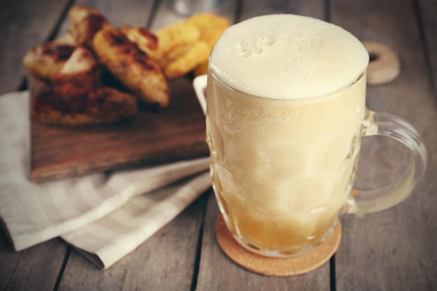 Glass of beer and chicken wings on wooden table close up