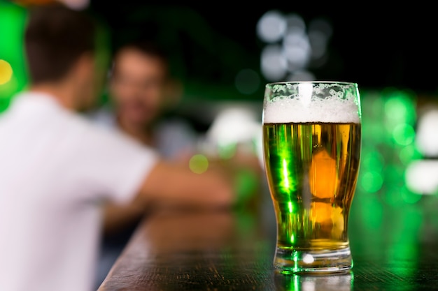 Glass of beer. Close-up of glass with beer on bar with people talking on the background