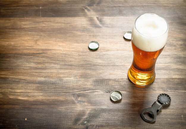 Glass of beer with stoppers and a bottle opener. On a wooden table.