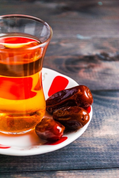 A glass of black tea and dates on a saucer