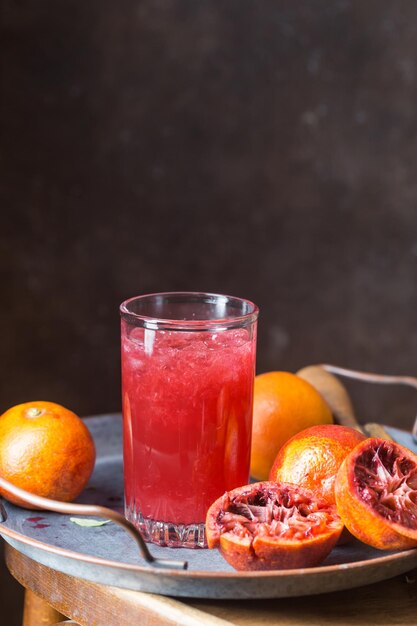 Glass of blood orange juice with ice and orange fruits on dark background