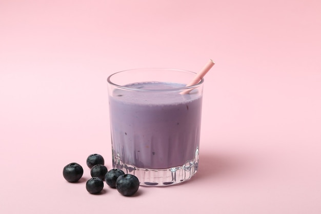 Glass of blueberry smoothie on pink background